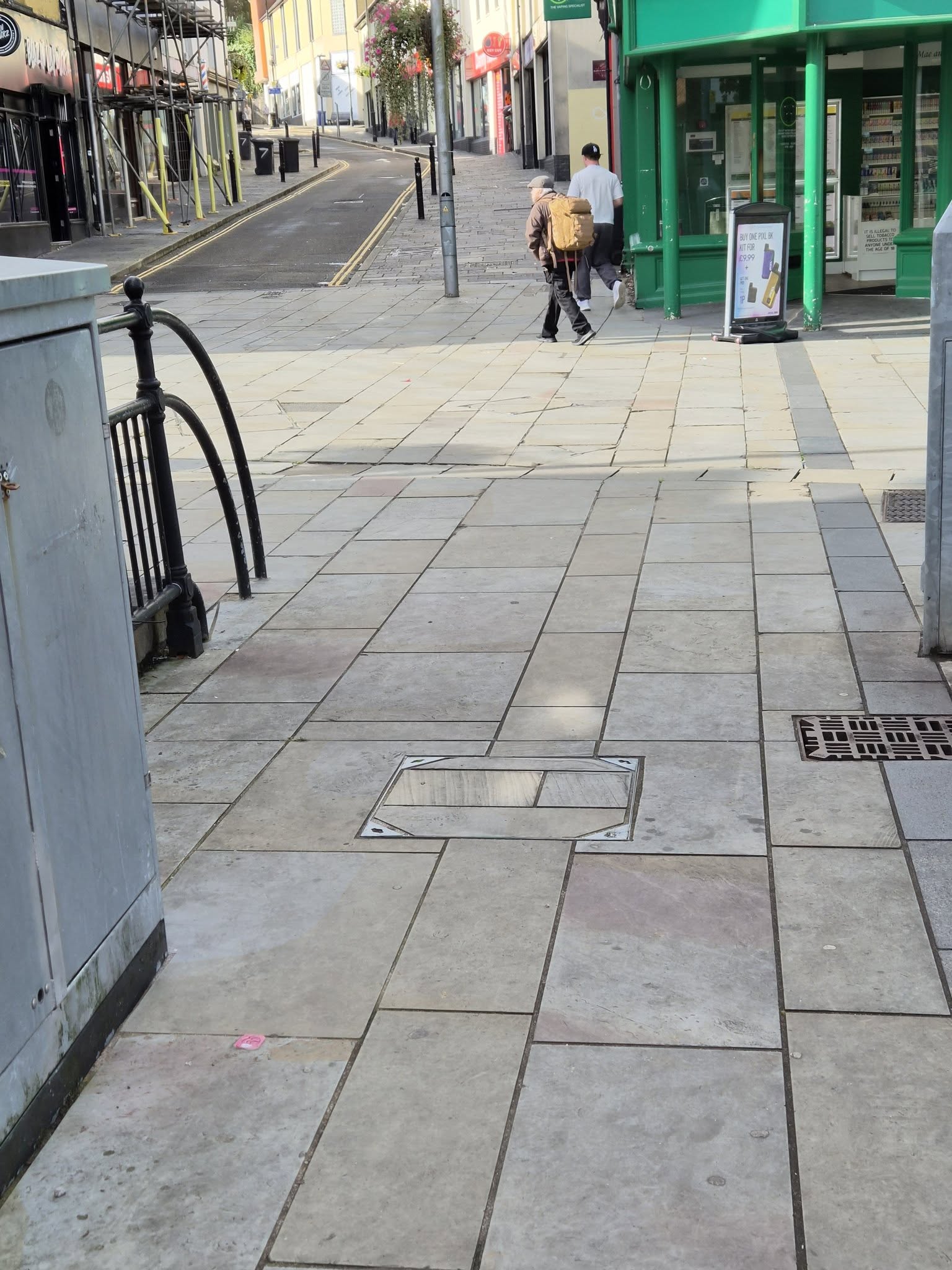 A man in a flat cap carrying a rucksack walking away from the premises through Pontypool town centre