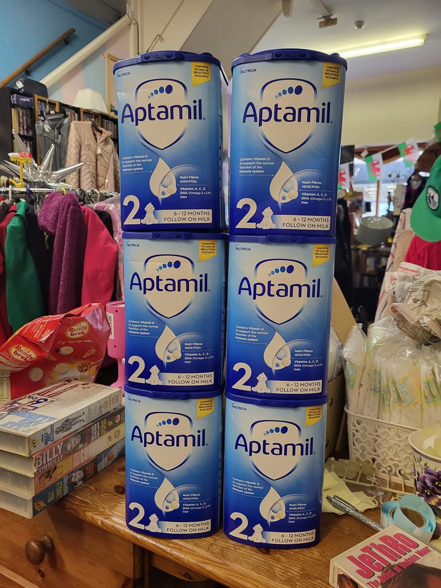 Six tins of Aptamil stage 2 follow-on milk stacked on a shop counter, posted with the caption 'Donated from a hospital partner'