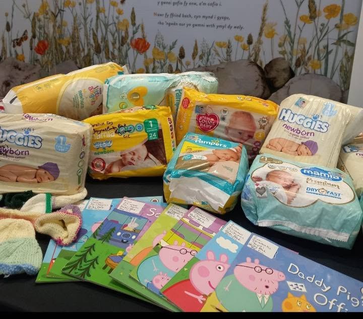 Packs of newborn nappies and Peppa Pig picture books laid out on a floral blanket, posted on 16 August 2026 with the note that they carry Jayne's Baby Bank stickers