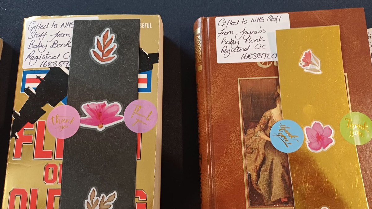 Two second-hand books with handwritten labels reading 'Gifted to NHS Staff from Jayne's Baby Bank Registered CIC 16838920', with stickers and bookmarks attached